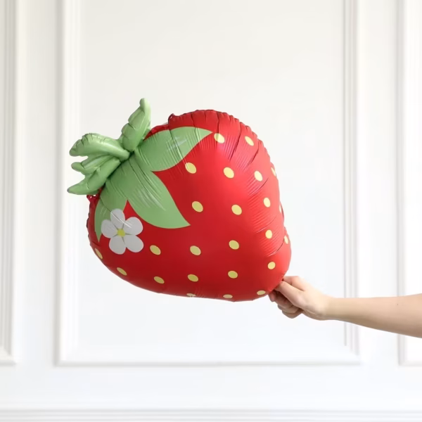 Balon din folie metalizata in forma de capsuna rosie cu seminte galbene frunze verzi si o floare alba izolat pe fundal alb