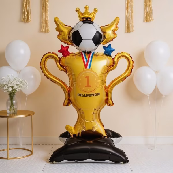 Balon Folie Airwalker Fotbal 96x54 cm Balon gigant din folie in forma de trofeu auriu cu numarul unu o minge de fotbal cu aripi si coroana asezat pe o baza neagra intr un decor elegant
