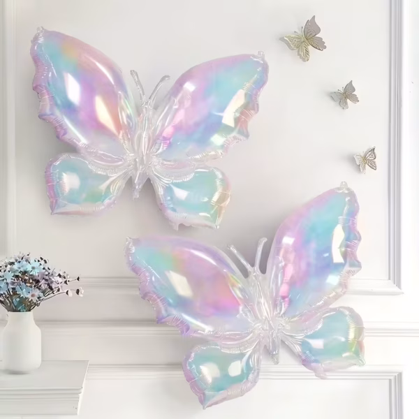 Doua baloane din folie in forma de fluture cu reflexii iridiscente asezate pe un perete alb decorat cu fluturi mici aurii