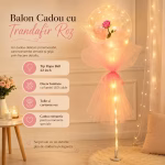 Balon transparent sferic iluminat cu LED uri ce contine un trandafir roz in interior fiind decorat cu tulle si panglica roz pe un suport de expunere