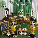 Balon airwalker cu tematica fotbal plasat langa o masa festiva bogat decorata cu un tort tematic briose si ghirlande verzi cu mesajul goal