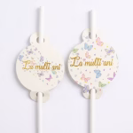 Paie decorative cu medalion La Multi Ani asezate pe o masa festiva alaturi de servetele pahare si un tort decorat cu fluturi