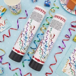 Tuburi cu confetti asezate pe un fundal albastru deschis decorat cu buline alaturi de fasii metalizate serpentine si pahare de petrecere