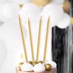 Set 12 Lumânări Aurii Elegante pentru Tort Patru lumânări aurii lungi și subțiri aprinse, așezate pe un tort elegant decorat cu bezele albe și praline aurii, pe un fundal festiv.
