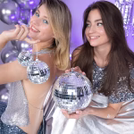 O tanara imbracata intr o rochie argintie stralucitoare tinand in maini un glob disco cu oglinzi intr un decor festiv cu baloane metalizate.