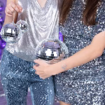 O tanara imbracata intr o rochie argintie stralucitoare tinand in maini un glob disco cu oglinzi intr un decor festiv cu baloane metalizate.