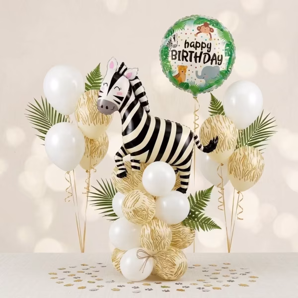 Aranjament spectaculos tip stand pe podea format din baloane latex albe si animal print alaturi de o figurina zebra din folie si un balon rotund happy birthday printre frunze tropicale