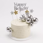 Tort alb decorat cu sfere argintii lucioase de diferite dimensiuni o coronita argintie tridimensionala stele cu sclipici argintiu si auriu si un topper argintiu cu mesajul Happy Birthday asezat central