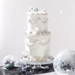 Set 8 Toppere Tort Glob Disco Argintii Tort alb etajat decorat elegant cu toppere in forma de glob disco argintiu asezat pe un suport din sticla.