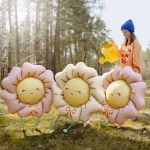 Balon din folie in forma de floare uriasa cu petale roz pastel un centru galben cu ochi inchisi obraji roz zambet raze aurii si o fundita aurie pe petala inferioara