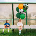 Balon din folie rotund avand un fundal cu model in sah in nuante de verde inchis si deschis decorat cu mingi de fotbal alb cu negru scheme tactice cu sageti albe si mesajul central Happy Birthday scris cu litere mari aurii