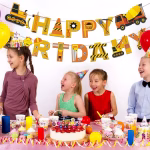 Banner festiv cu mesajul Happy Birthday, suspendat deasupra unei mese de petrecere pentru copii, având literele decorate creativ cu motive de șantier, utilaje, dungi de avertizare și unelte