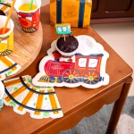 Set de 6 farfurii din carton decupate in forma de locomotiva de tren cu aburi in trei culori asortate menta galben si rosu cu inscriptia Happy Express