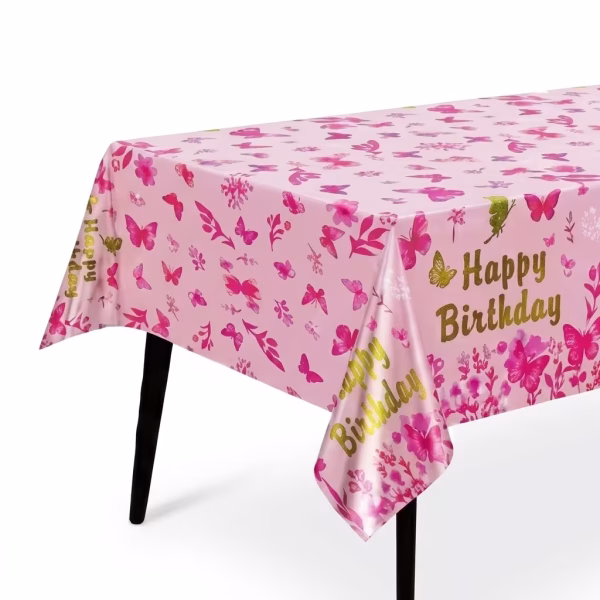 Fata de masa dreptunghiulara de culoare roz deschis decorata pe toata suprafata cu fluturi si motive florale roz intens si marginita de mesajul aurit Happy Birthday