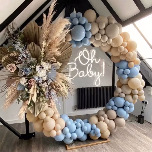 Arcadă organică din baloane montată pe un suport circular, combinând elegant nuanțe pastelate de bleu macarons, bej și alb nisipiu, decorată asimetric și acompaniată de un aranjament floral cu pampas