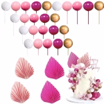 Tort alb decorat cu aplicatii florale, pus in valoare de o cascada eleganta din sfere aurii, albe, roz pal si roz inchis, alaturi de frunze evantai pliate in partea superioara in nuante asortate de roz
