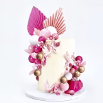 Tort alb decorat cu aplicatii florale, pus in valoare de o cascada eleganta din sfere aurii, albe, roz pal si roz inchis, alaturi de frunze evantai pliate in partea superioara in nuante asortate de roz