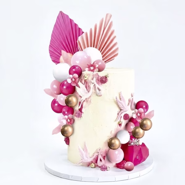 Tort alb decorat cu aplicatii florale, pus in valoare de o cascada eleganta din sfere aurii, albe, roz pal si roz inchis, alaturi de frunze evantai pliate in partea superioara in nuante asortate de roz