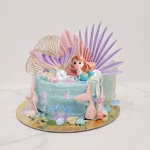 Tort decorat cu tematica marina incluzand o figurina sirena 3D, cozi de sirena, perle, scoici, frunze evantai pastelate si elemente aurii