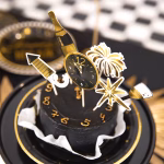 Set de 6 toppere din carton pentru tort de Revelion, ilustrând elemente festive minimaliste în culorile negru și auriu: o sticlă de șampanie cu textul Cheers, o explozie de artificii, un pahar elegant de șampanie, o rachetă de artificii, o stea cu opt colțuri și un ceas care indică miezul nopții