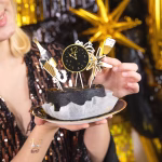 Set de 6 toppere din carton pentru tort de Revelion, ilustrând elemente festive minimaliste în culorile negru și auriu: o sticlă de șampanie cu textul Cheers, o explozie de artificii, un pahar elegant de șampanie, o rachetă de artificii, o stea cu opt colțuri și un ceas care indică miezul nopții