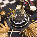 Set de 6 toppere din carton pentru tort de Revelion, ilustrând elemente festive minimaliste în culorile negru și auriu: o sticlă de șampanie cu textul Cheers, o explozie de artificii, un pahar elegant de șampanie, o rachetă de artificii, o stea cu opt colțuri și un ceas care indică miezul nopții