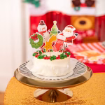 Set de 6 toppere din carton pentru tort, ilustrând figurine clasice de Crăciun: o șosetă roșie decorată, un brad împodobit cu o stea în vârf, Moș Crăciun zâmbitor, o stea căzătoare zâmbitoare, un om de zăpadă cu fular roșu și o coroniță verde cu fundă roșie