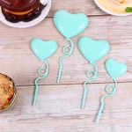 Set de 4 toppere din plastic lucios in forma de inimi tip balon de culoare turcoaz, prevazute cu tije ondulate ce imita panglicile, asezate ca decor pe un tort asortat in aceeasi nuanta