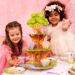 Suport etajat tridimensional din carton sub forma unui copac magic cu trei niveluri verzi ilustrand o casuta de poveste decorata cu zane fluturi un melc roz ciupercute rosii ferestre luminate si o carare de piatra