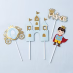 Set de 4 toppere din carton pentru tort cu tematica Micul Print, incluzand un castel albastru cu accente aurii, o caleasca, figurina print cu pelerina rosie si textul Prince cu coronita, montate pe bete albe de sustinere